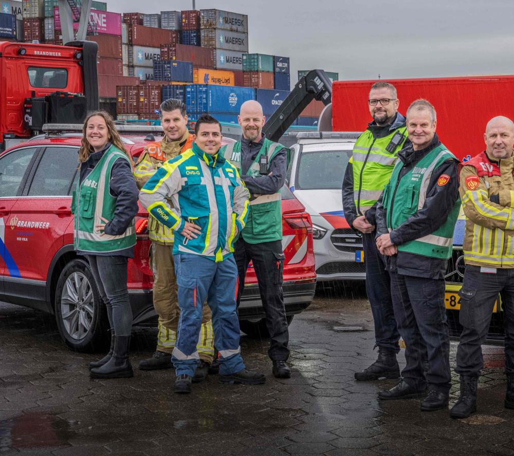 Foto op havenkade in Venlo met containers op de achter. Voertuigen van brandweer, politie en geneeskundige zorg. Daarvoor staan 8 collega's. Onder andere Bevelvoerder OvD G. 